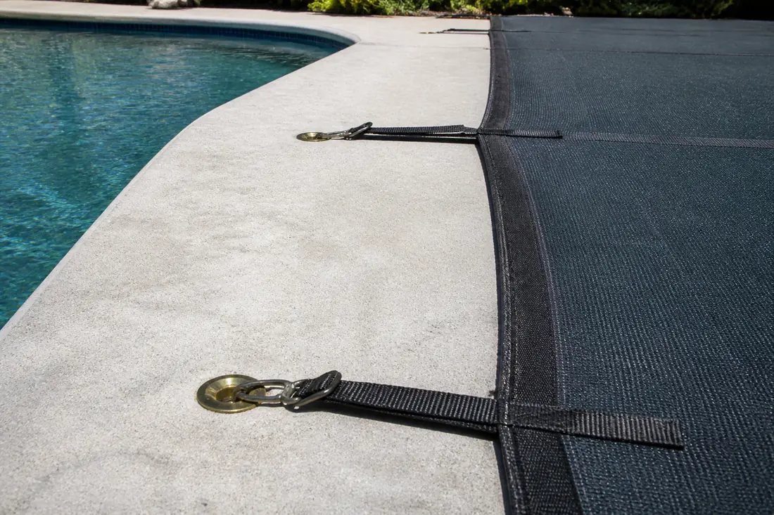 Brass anchor points set flush into a pool deck with safety cover straps hooked into them