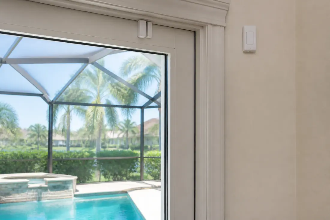 A door alarm contact sensor at the top of a sliding glass door onto a pool deck