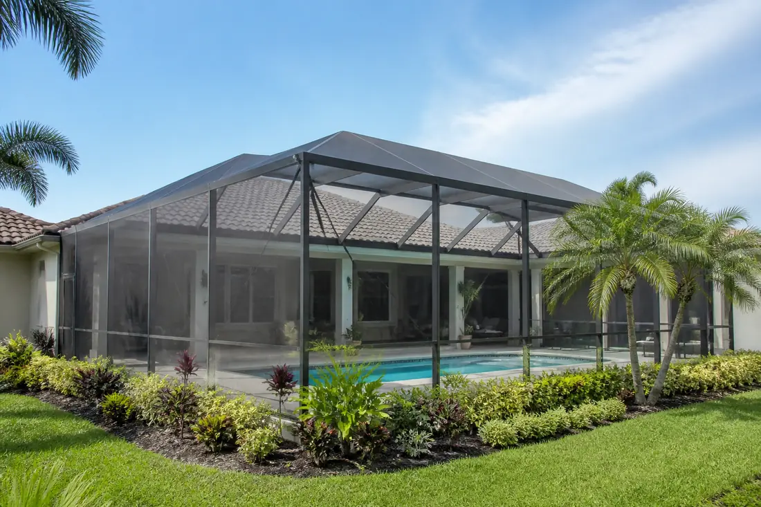 A screened pool enclosure attached to a Florida home, seen from the yard with the pool visible through the mesh