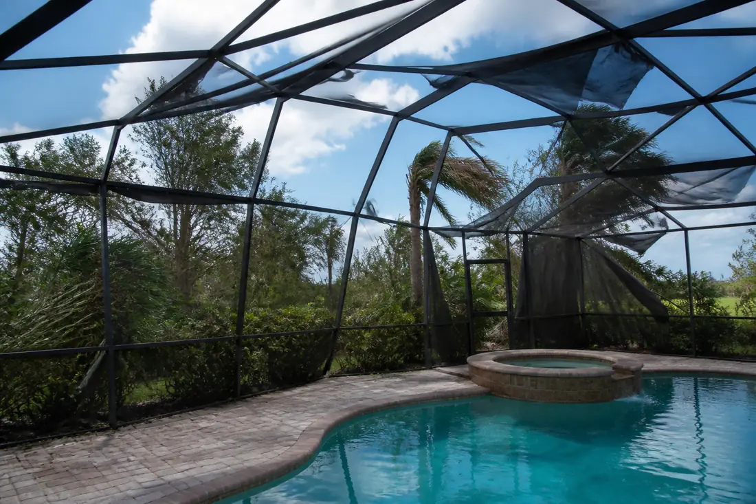 A storm-damaged pool enclosure with bent framing and torn screens